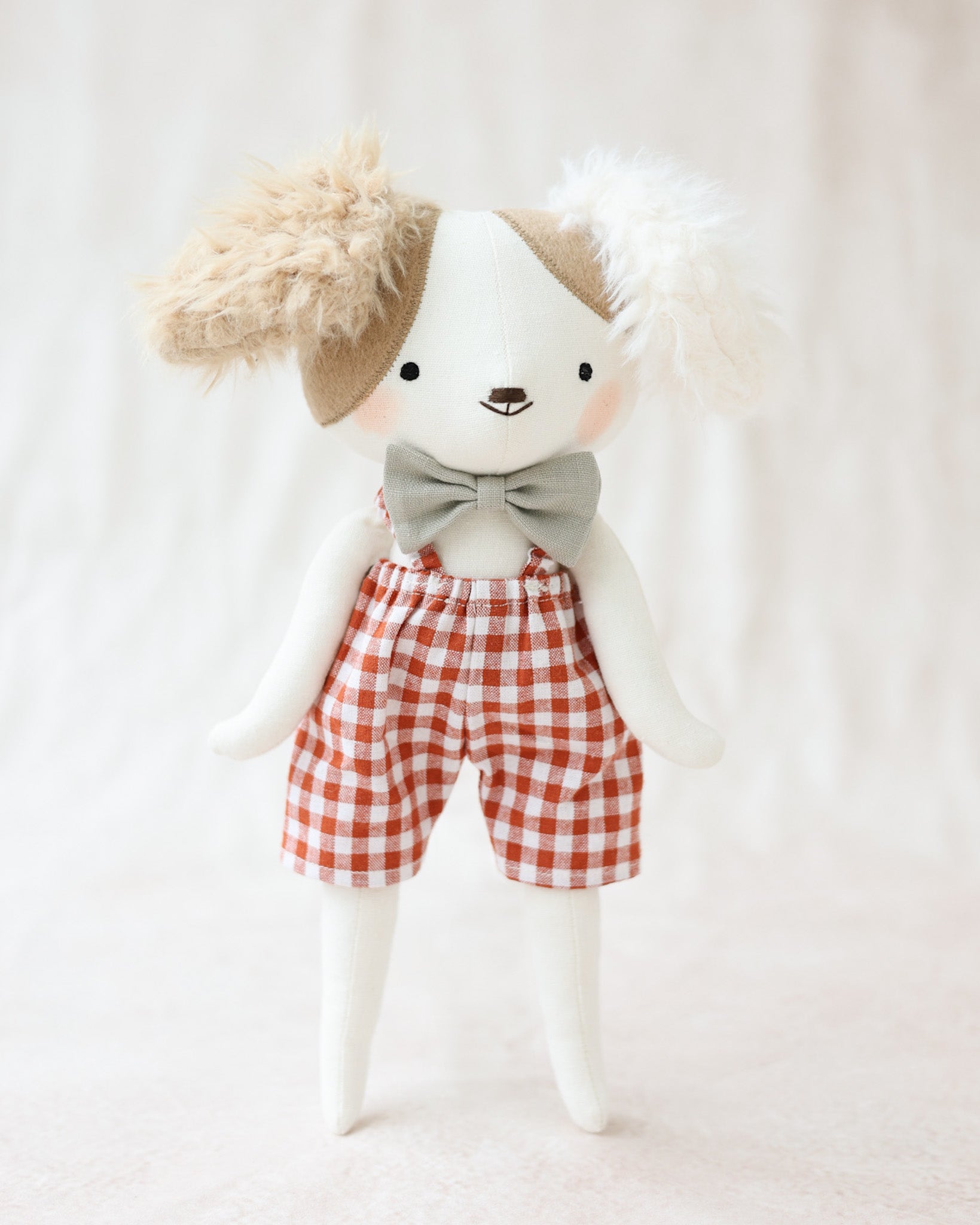 赤いギンガムチェックのジャンプスーツと蝶ネクタイを着た犬のぬいぐるみアルフォンス